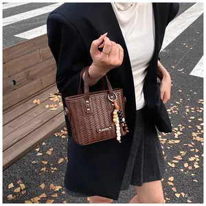 Detail der dunkelbraunen Webstruktur-Handtasche mit Perlenanhänger auf Außenbank