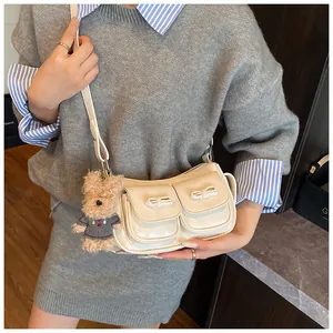 Detail der cremefarbenen Schultertasche mit Schleifentaschen und süßem Bären-Anhänger