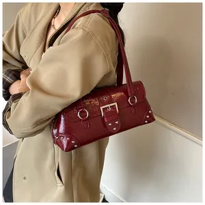 Close-up of wine red patent leather shoulder bag with metallic rivets and silver buckle