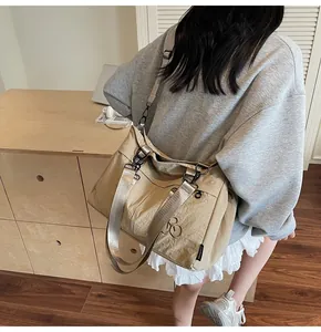 Close-up of khaki nylon crossbody bag with dual-ring metal logo and wide strap detail