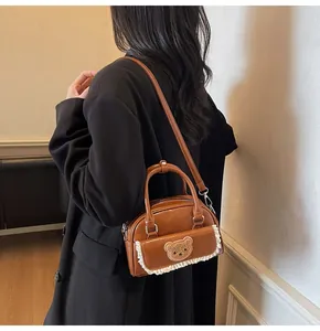 Detail einer braunen PU-Ledertasche mit gesticktem Bären und weißem Spitzenbesatz