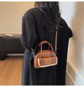 Detailansicht der braunen Mini-Boston-Tasche mit Bären-Patch und feinem Spitzenbesatz