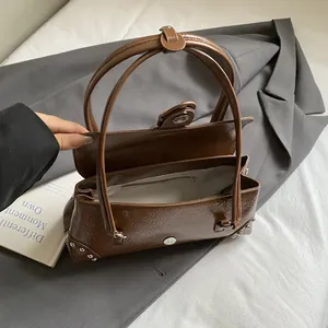 Brown vintage faux leather underarm bag with silver rivets on grey blazer background