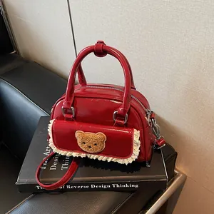 Rote Lacklederhandtasche mit Bären-Aufnäher und Spitze auf einem Design-Buch