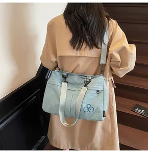 Detail of light blue nylon bag featuring an embroidered logo and thick shoulder strap