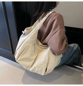 Detail of cream nylon dumpling bag featuring multiple functional front pockets and wide strap