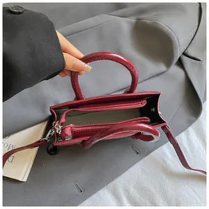 Top view of burgundy square bag with interior zipper pocket on a grey blazer