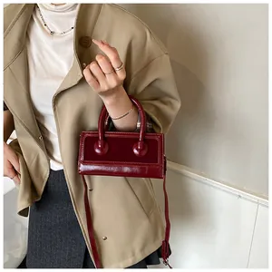 Detail of burgundy mini square bag featuring patent leather texture and velvet stitching