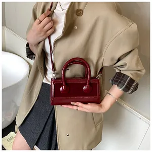 Detail of burgundy patent leather handbag with glossy finish and silver hardware on a coat