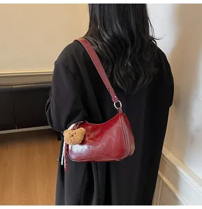 Detail of dark red underarm bag featuring a plush bear charm and glossy finish