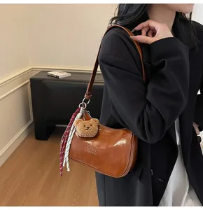 Detail of a brown glossy leather shoulder bag featuring a bear charm and brand logo