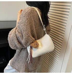 Detail of white leather underarm bag with cute bear charm and tassel on a stylish model