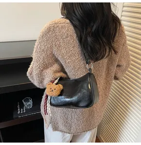 Detail of black semi-circle bag with teddy bear charm and striped ribbon on sweater