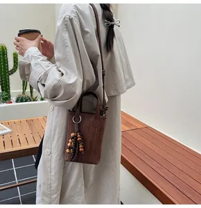 Close-up of brown textured crossbody bag with decorative wood beads and leather strap