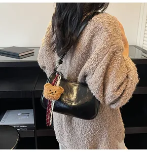 Detail of black glossy crescent bag with plush bear charm and striped scarf accessory