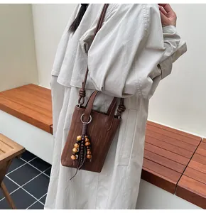 Detail of a brown woven crossbody bag with wood bead tassel and knot strap on a trench coat