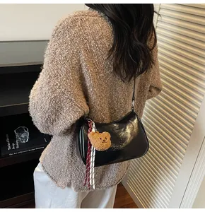 Detail of a black glossy hobo bag with a cute brown plush bear charm and thin strap