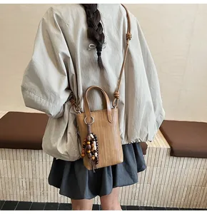 Detail of a brown woven mini crossbody bag with wooden bead charm and knotted strap design