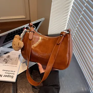 Vintage brown leather shoulder bag with plush bear charm against a minimalist home background