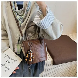 Detail view of woven leather bucket bag with colorful wooden bead tassel and logo strap