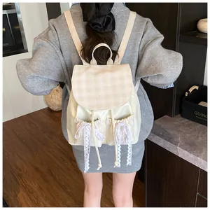 Detail of cream backpack featuring plaid flap and white lace bow decoration in soft lighting