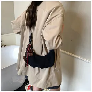 Détail du sac hobo noir avec bandoulière nouée et pendentifs sur un trench-coat kaki