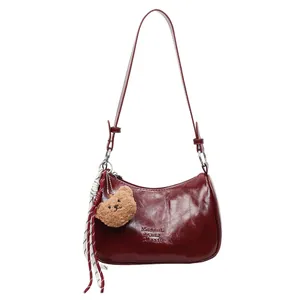 Deep red leather underarm pillow bag with plush bear charm and woven strap detail
