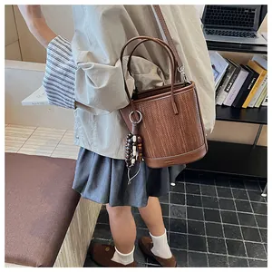 Detail of woven brown bucket bag with beaded charm and embossed brand logo on base