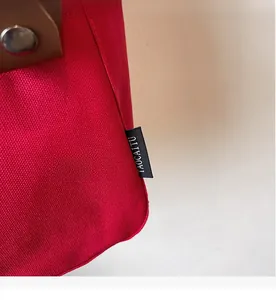 Detail of red canvas tote bag with woven brand label and leather strap with metal snap