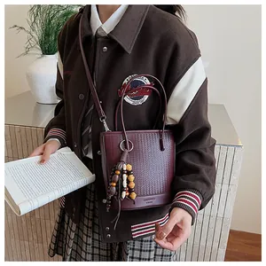 Detail of woven burgundy bucket bag featuring a wood bead tassel and logo engraving