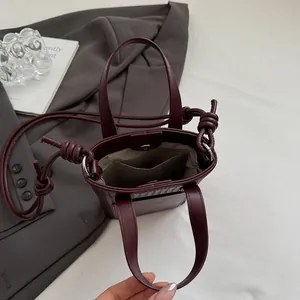 Deep wine red mini crossbody bucket bag with knot detail on grey blazer backdrop