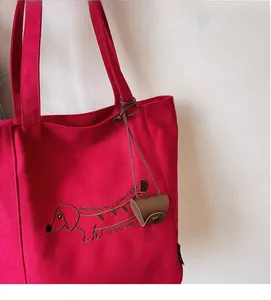 Detail of red canvas tote bag with dachshund embroidery and attached leather charm accessory