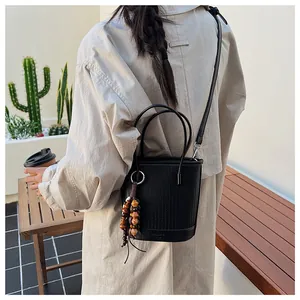 Detail of black bucket bag with woven texture, round handles and wooden bead tassel charm
