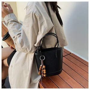 Detail of black woven bucket bag with elegant wooden bead tassel and smooth leather base