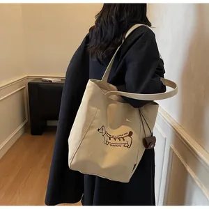 Close-up of beige canvas tote with embroidered dachshund and small leather charm bag