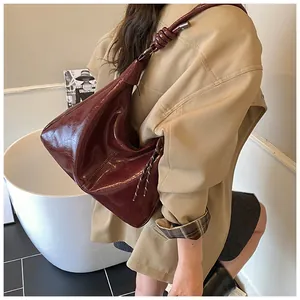 Détail du sac hobo en cuir brillant bordeaux avec nœud décoratif sur la bandoulière
