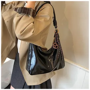 Détail du sac croissant noir brillant avec bandoulière nouée et breloque bretzel porté
