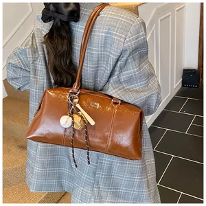 Detail der braunen Vintage-Glanzledertasche mit Golf-Text und Baseball-Anhänger