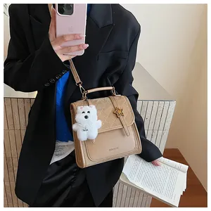 Detail einer beigen gesteppten PU-Lederhandtasche mit Stern- und Plüschhund-Anhänger