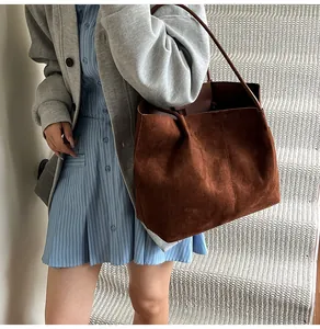 Detailed texture of a large dark brown suede tote bag with vertical stitching and thin strap