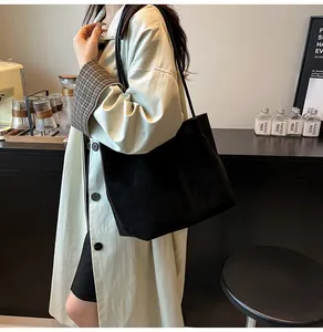 Close-up of a minimalist black suede tote bag shown on a model in a stylish indoor setting