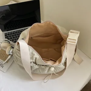 Geräumige beige Nylon-Umhängetasche mit Falten auf Schreibtisch neben Laptop-Zubehör