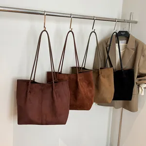 Large suede tote bag in four autumn colors hanging on a metal rack in a studio