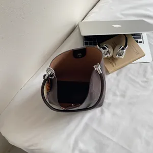 Sac seau en cuir marron avec fermeture magnétique sur un lit à côté d'un ordi