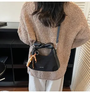 Detail of black crescent dumpling bag featuring bow handle and decorative wooden beads
