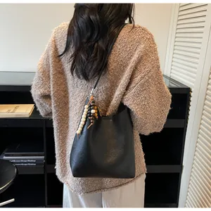 Détail du sac hobo en cuir noir avec charm en perles de bois tricolores sur la bandoulière