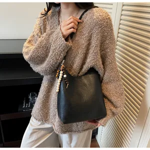 Détail du sac à bandoulière noir avec breloque perlée vintage et logo embossé élégant