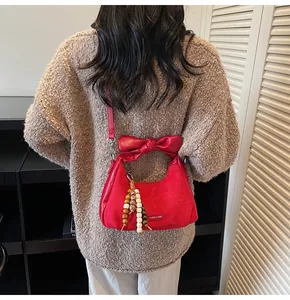 Detail of red suede dumpling bag featuring a decorative bow handle and beaded tassel