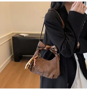 Detail of a brown matte leather bag with a stylish bow handle and beaded fringe charm