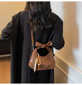 Detail of brown suede dumpling bag with a decorative bow handle and beaded charm